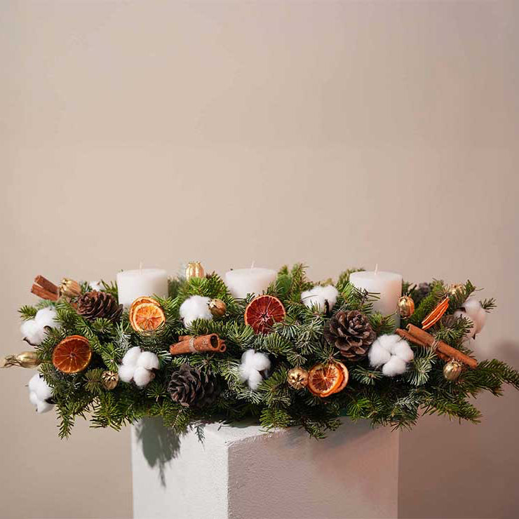 Decorative arrangement with candles, pinecones, and other elements on a plain background