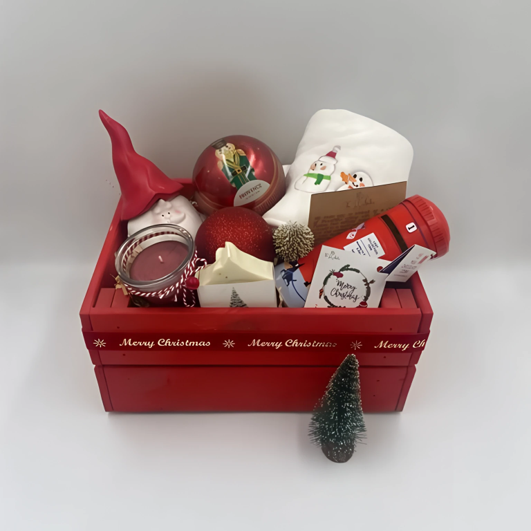 A Wooden festive hamper, red color, having Christmas towel, a ball Christmas ornament with tea bags inside, candle, porcelain Santa's container, natural handmade festive soap bar with Christmas tag, Christmas chocolate