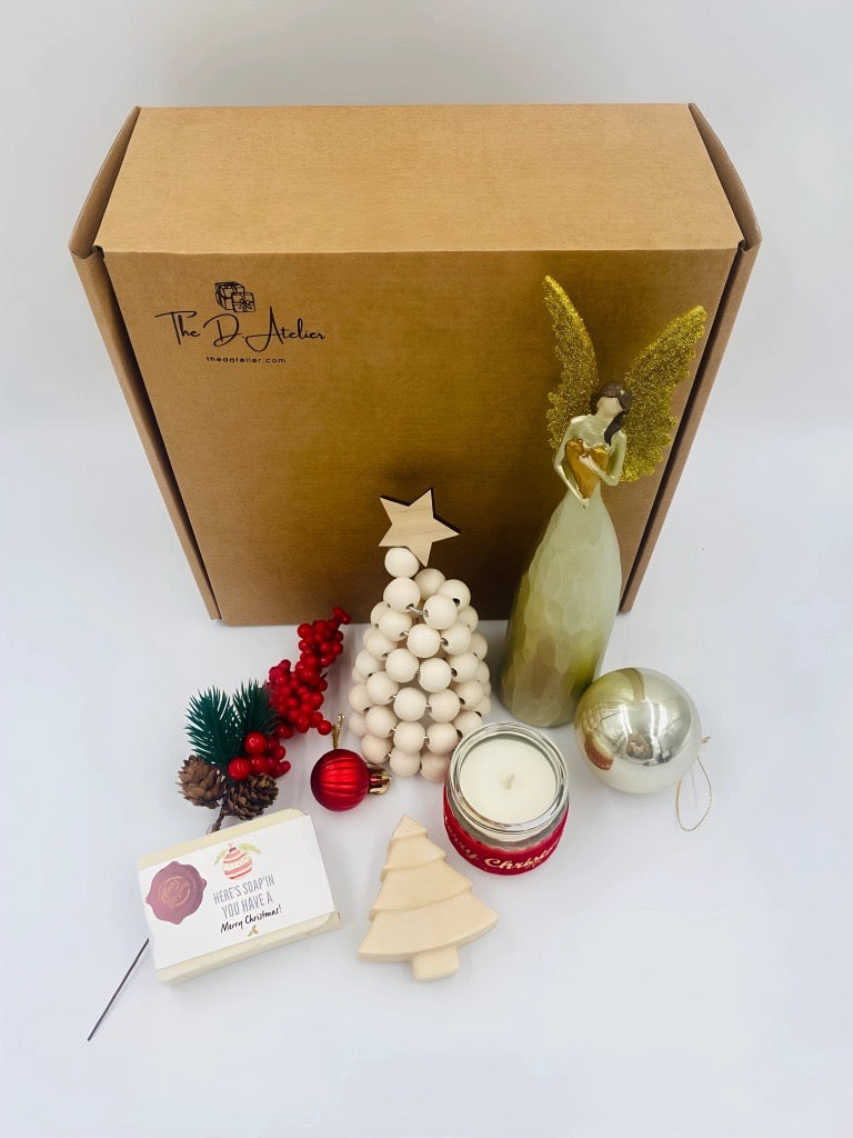 Decorative items including a wooden Christmas tree, candle, and angel figurine in front of a branded box.