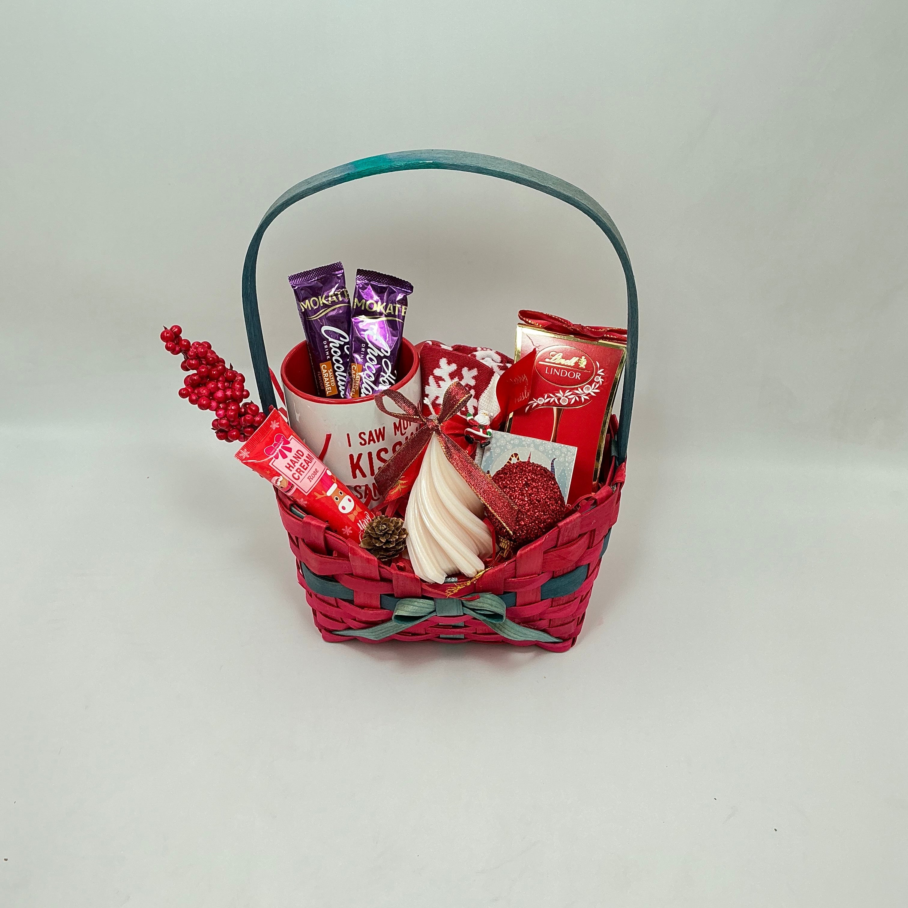 Basket with red and white decorative items and a purple chocolate bar on a light gray background