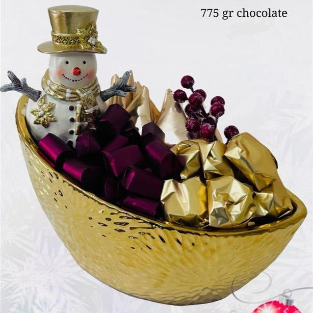 Decorative gold bowl with a snowman figurine, purple bows, and gold-wrapped chocolates on a white background.