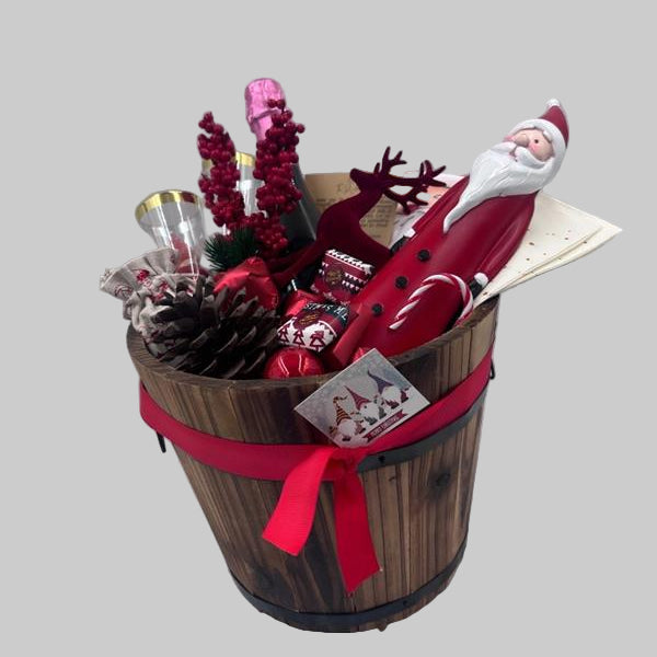 A gift basket featuring a Santa Claus figure, a velvet reindeer, sparkling non-alcoholic champagne, festive chocolates, a pine cone, two champagne flutes, a jute bag, Christmas ornaments, kitchen towels, and two festive Christmas napkins.