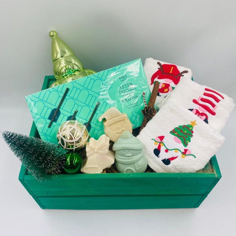 Decorative Christmas items including a green wooden box, small tree, Chocolate Batons box, Christmas towels, natural handmade soaps, and Christmas ornaments 