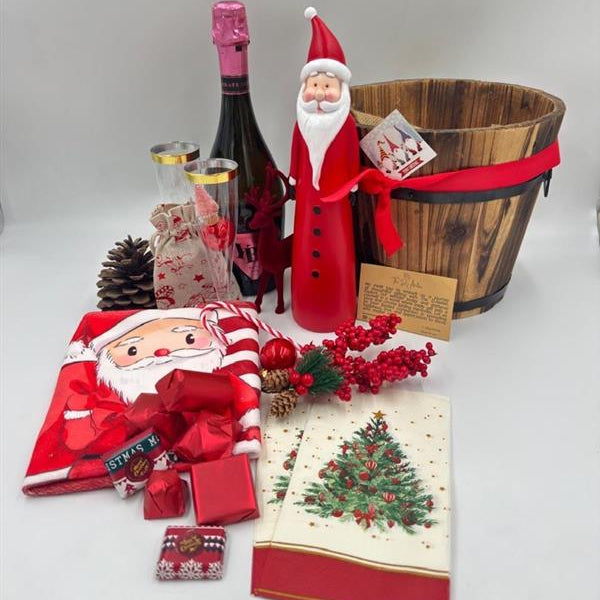 A gift basket featuring a Santa Claus figure, a velvet reindeer, sparkling non-alcoholic champagne, festive chocolates, a pine cone, two champagne flutes, a jute bag, Christmas ornaments, kitchen towels, and two festive Christmas napkins.