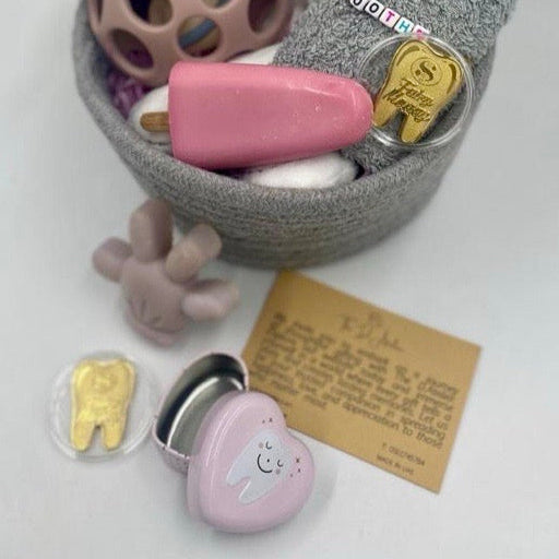 Gray woven basket with toys and a plush bear, Small heart-shaped container with gold tooth model, pink object, Squishy toy. natural handmade soaps, small face towel.