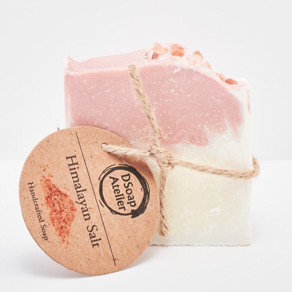 A bar of Himalayan Salt Natural Handmade Soap with a white base and pink top, tied with a string next to a label that reads 'Himalayan Salt'. The soap is on a white background. Front side of the soap. 
